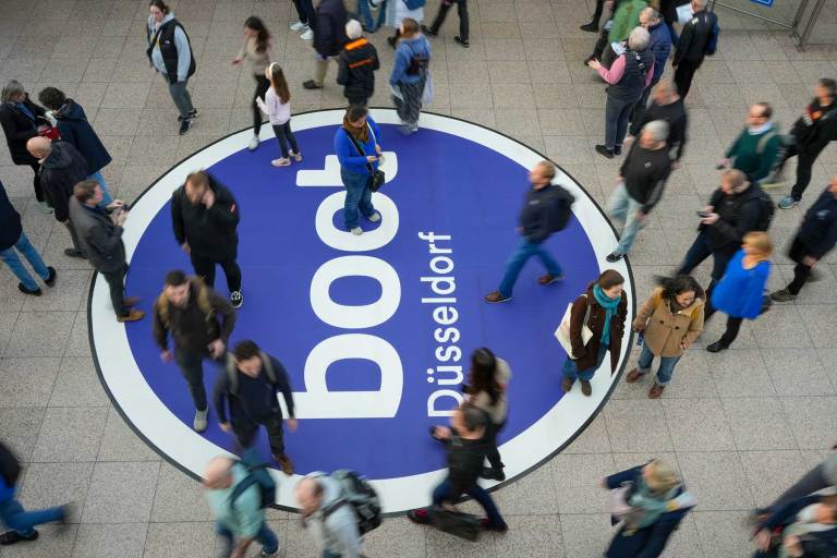 1_BOOT-260618 People walking in a room with a large blue logo on the floor