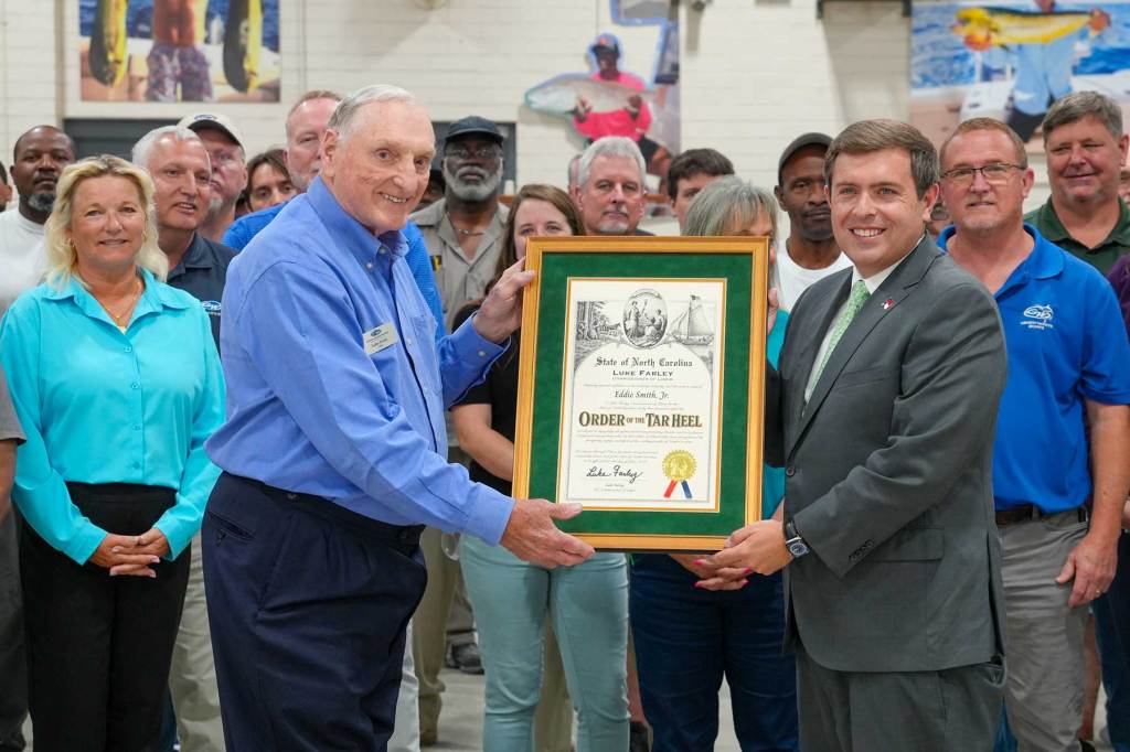 The focus on two men with an awards frame being held by both of them surrounded by on lookers