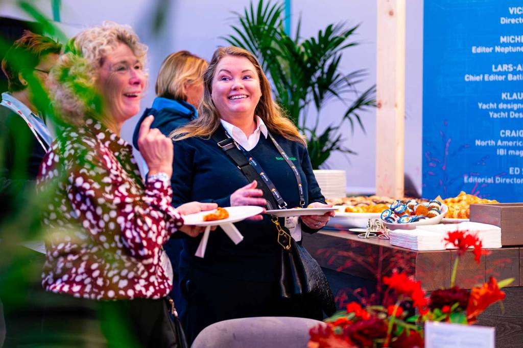 Two women in an image laughing and eating at a conference.